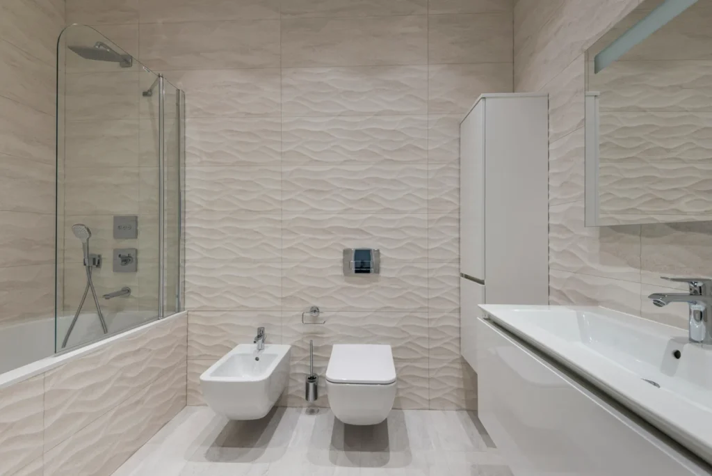 Modernes Bad mit Wellenfliesen, Bidet und klappbarer Glas-Duschabtrennung mit Regendusche.