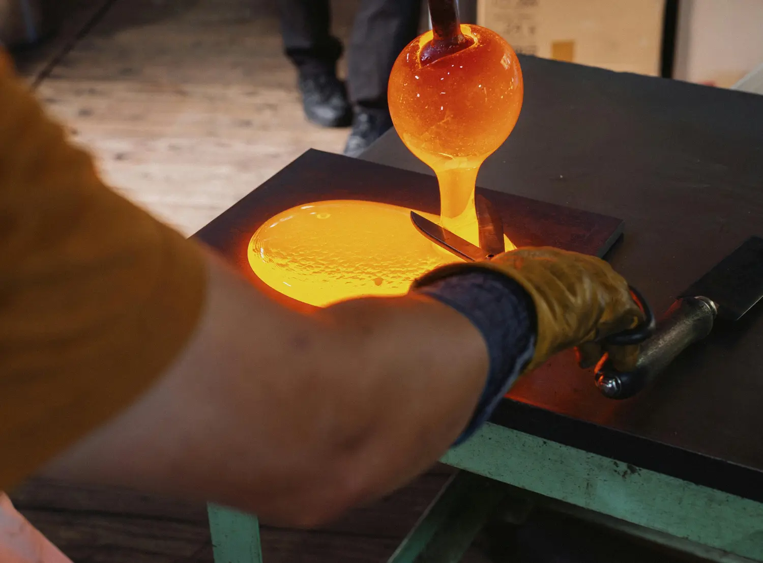 Ein Glasmacher bläst mit der Glasmacherpfeife einen glühenden Zylinder aus Glas.